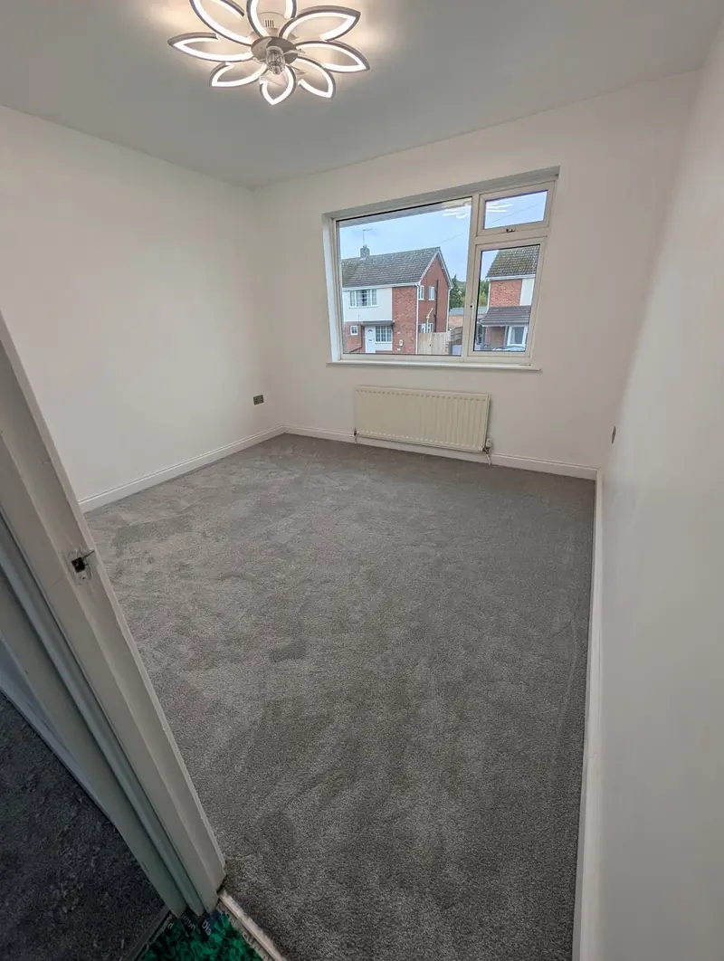 Grey carpet in a smaller bedroom with a window looking onto houses opposite.