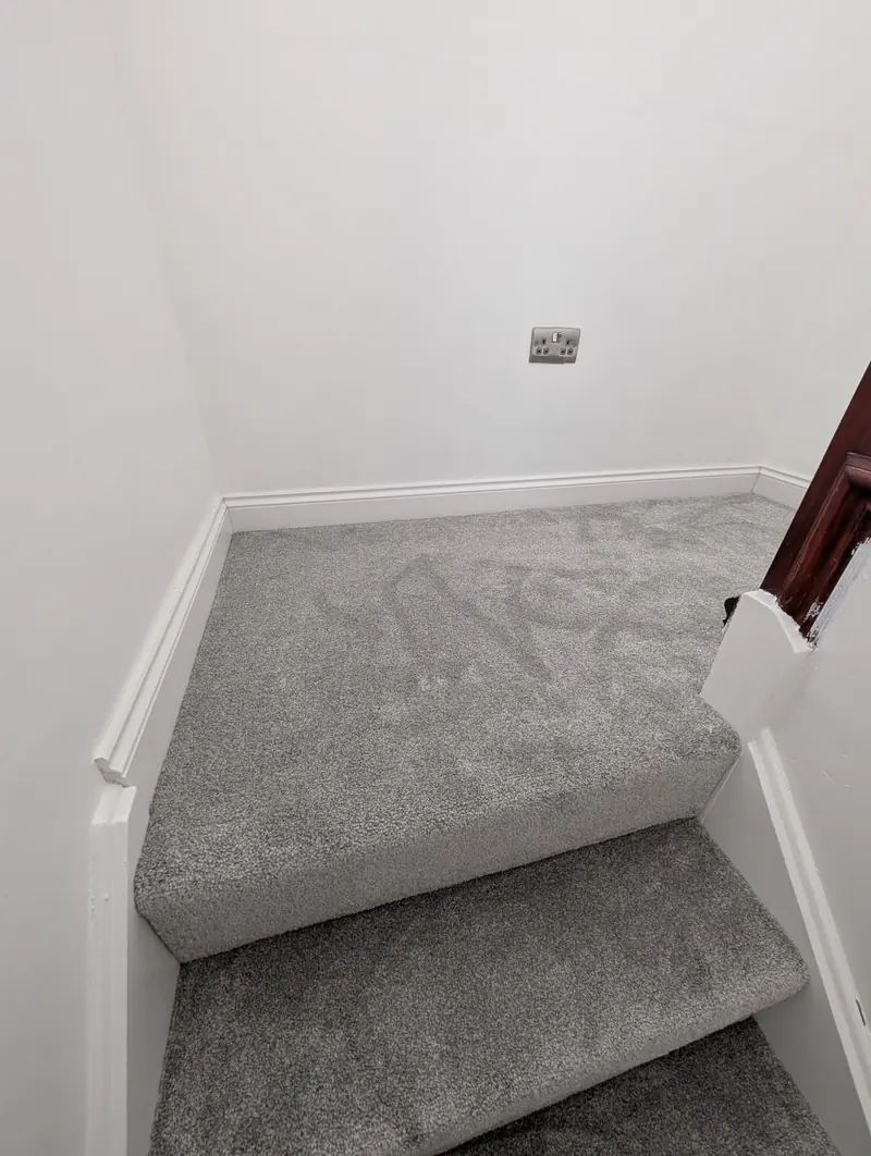 Grey carpet finished neatly at the top of a flight of stairs where it meets the landing.