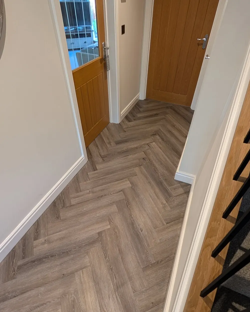 Grey herringbone LVT in a hallway, running past an oak door and the foot of a staircase.
