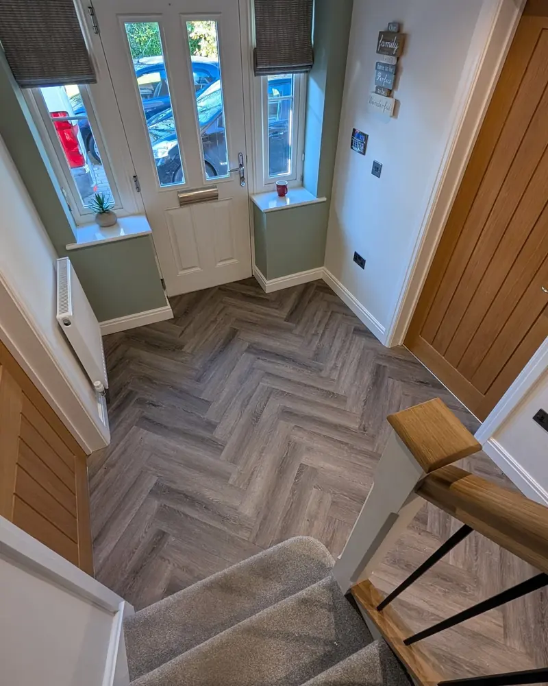 Grey herringbone LVT laid into a porch with green walls, a window seat and a white front door.