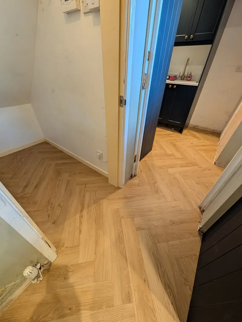 Natural oak herringbone running through a doorway, with the pattern kept square across the threshold.