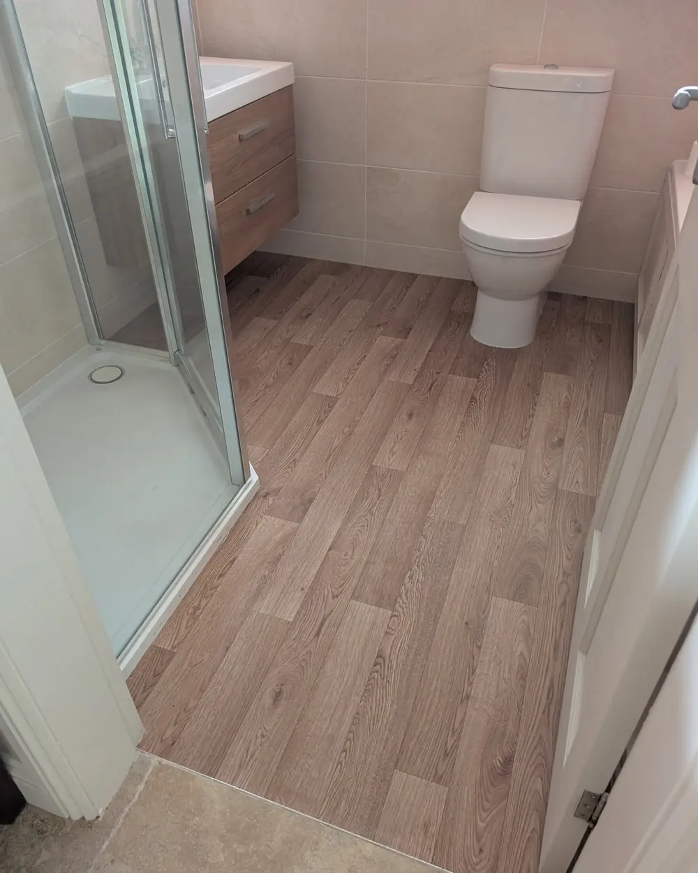 Pale wood effect plank flooring in a bathroom, fitted around a shower tray and a wall hung vanity.