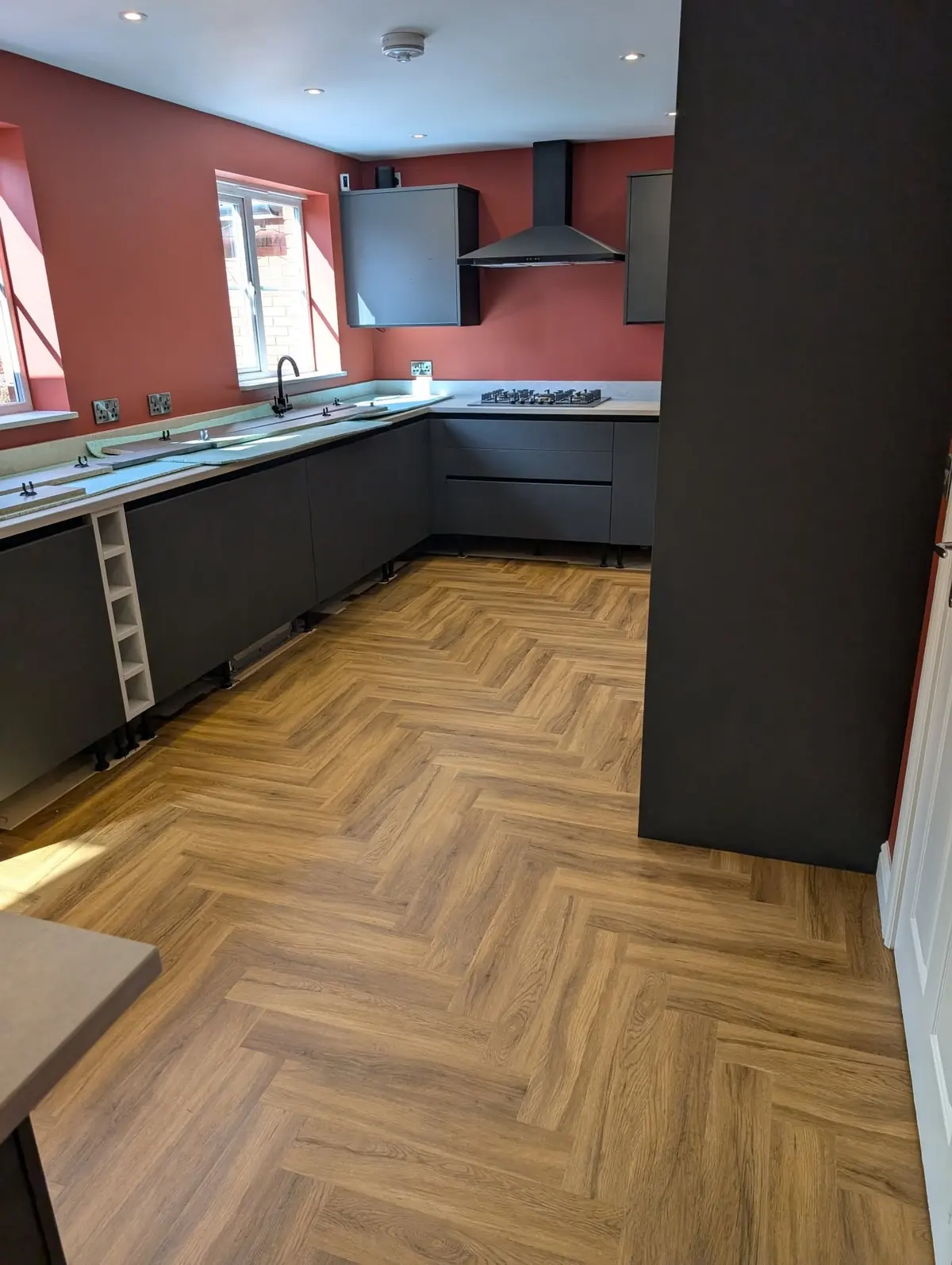 Walnut herringbone LVT in a kitchen with terracotta walls, dark grey units and a chimney extractor.