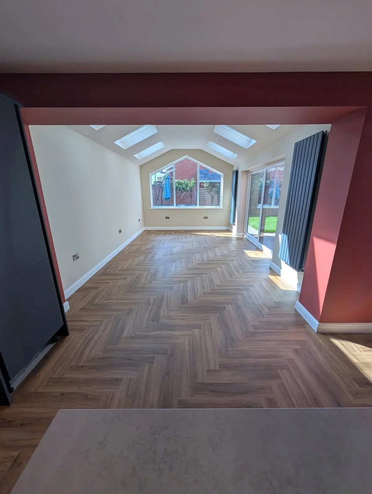 Walnut herringbone LVT running through an open plan kitchen extension with a terracotta feature wall and a vaulted apex window.