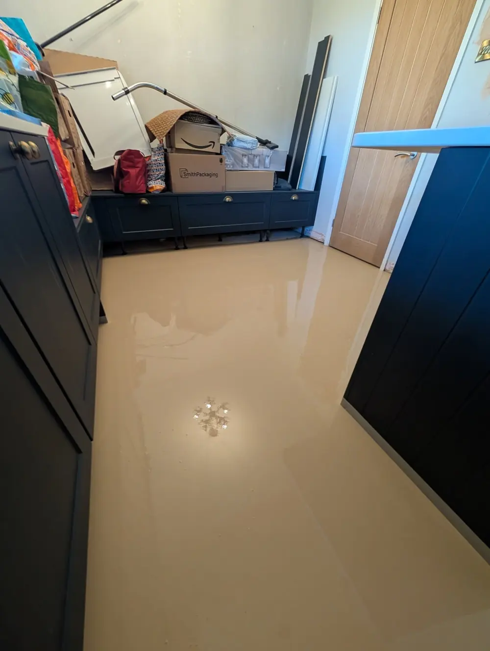 Wet cream latex screed poured across a kitchen floor between navy units, still glossy.