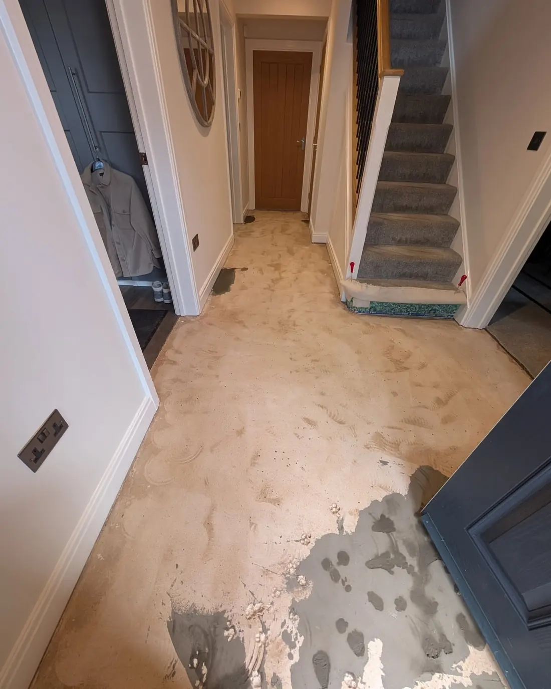 A hallway floor part covered in cream levelling compound, patchy where it has been worked into low spots.