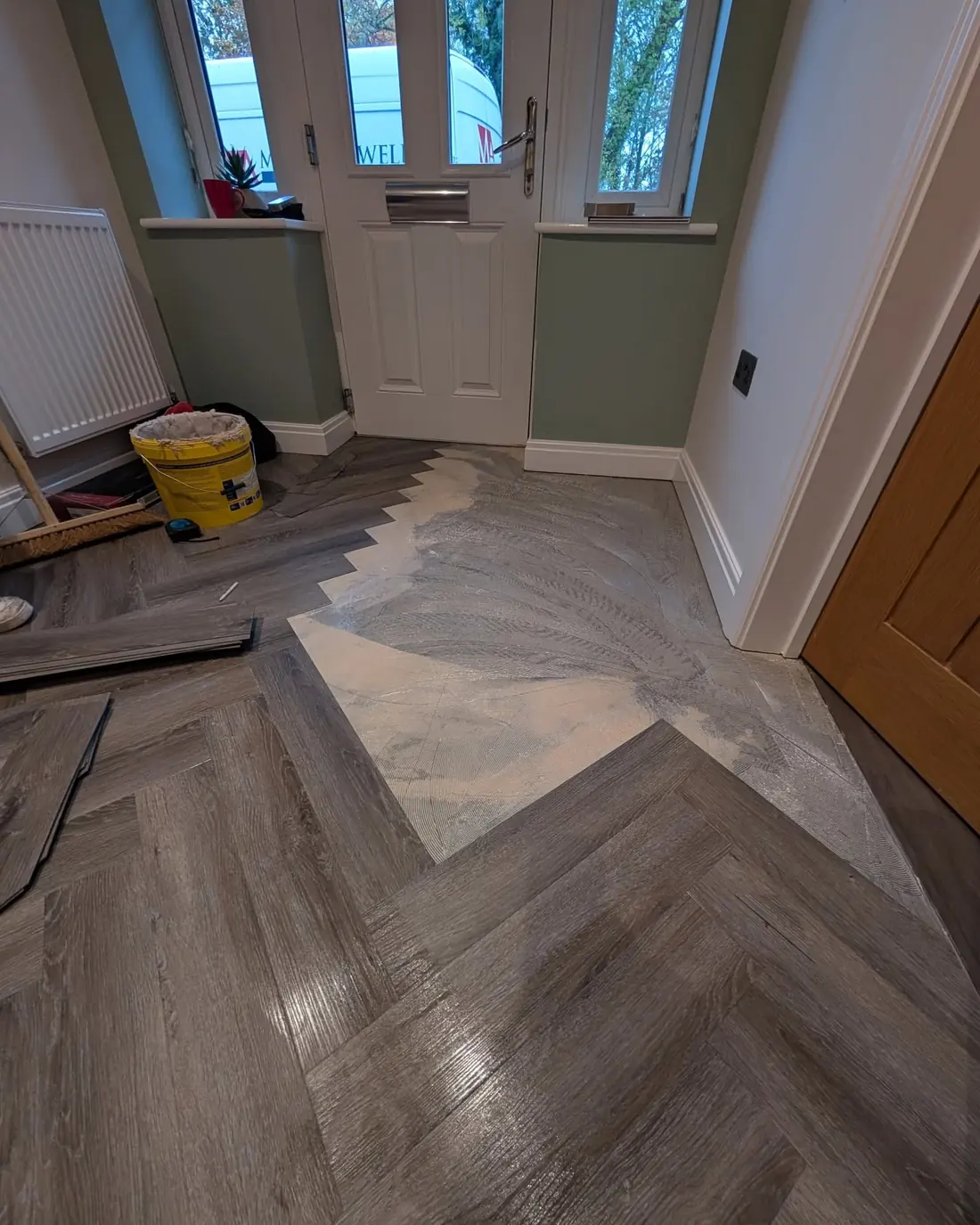 Grey herringbone LVT part laid in a hallway with a bare patch of sub floor still showing.