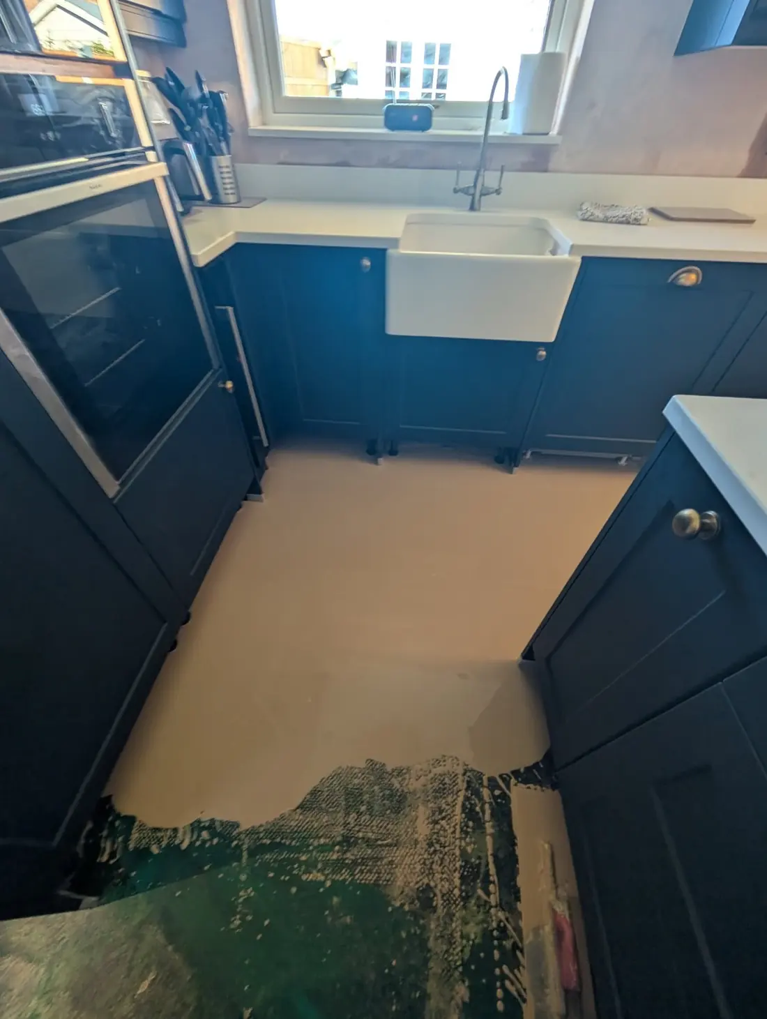 Navy kitchen with a white Belfast sink. The old floor covering is coming up and a green residue is still stuck to the boards in the corner.
